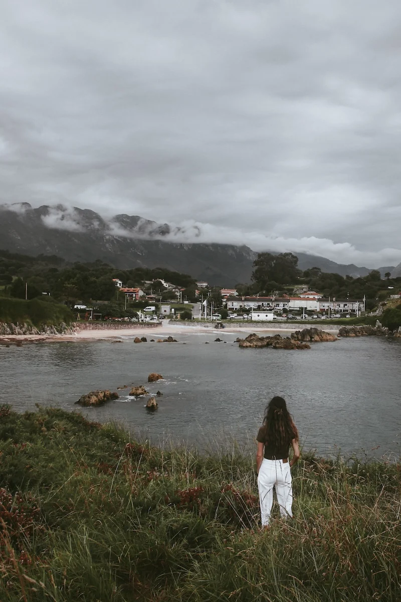 Mujer contemplando la Playa de Toró y el paisaje montañoso de fondo, en Llanes, Asturias